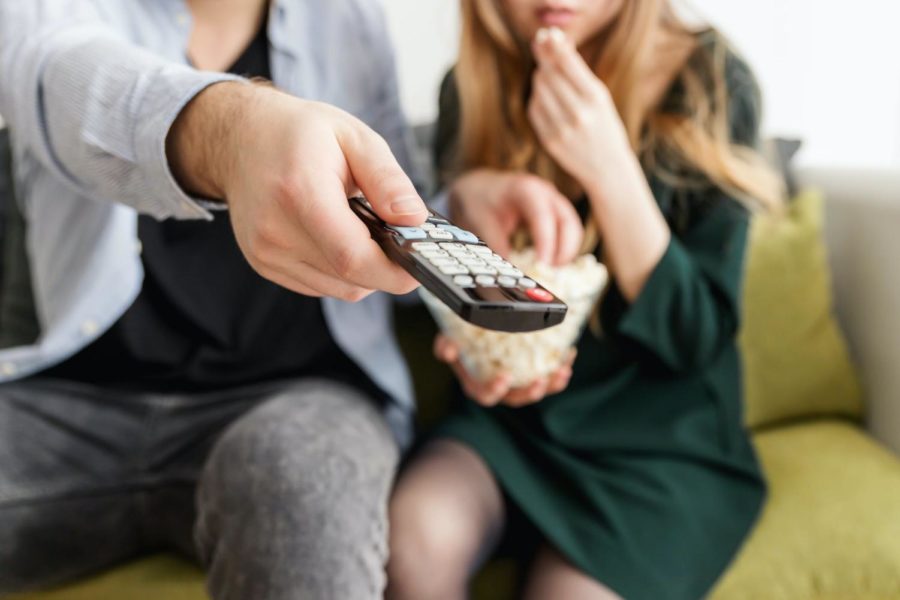 A couple watching television while the man points remote at screen to change the channel