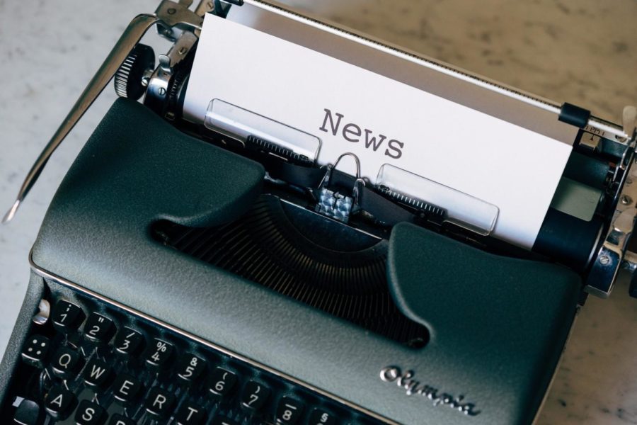 A typewriter printing out paper which contains a news story