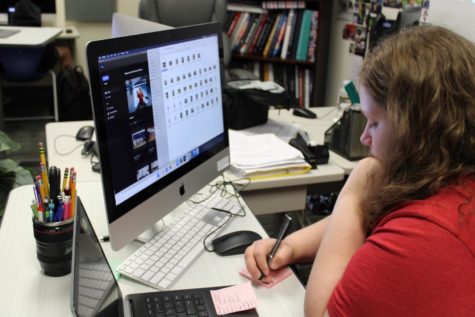Yearbook student working with images on laptop and writing on sticky note